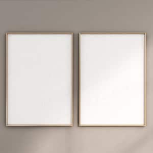 Può includere: Due stampe artistiche rettangolari bianche e vuote in cornici dorate sono esposte fianco a fianco contro un muro dai toni neutri. Le cornici hanno un sottile bordo dorato. Il muro ha una consistenza sottile e un'ombra della luce solare.