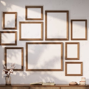 May include: A white wall with nine gold picture frames of various sizes. The frames are empty and arranged in a staggered pattern.
