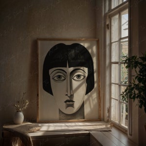May include: A framed black and white art print featuring a stylized portrait of a woman with a bob haircut. The artwork is displayed on a windowsill, next to a window with natural light.