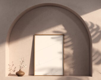 May include: A light brown, ceramic vase with a small bouquet of white flowers sits on a shelf in a niche. The niche is framed by a rounded archway. A gold frame with a blank white canvas hangs on the wall behind the vase.