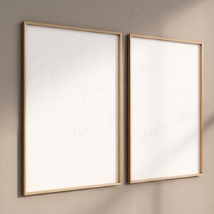 May include: Two empty picture frames with a light brown wood frame and white matting. The frames are hanging on a beige wall.