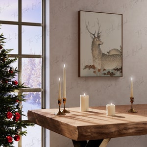 May include: A wooden table with four lit candles and a framed print of a deer in a forest setting. The table is in front of a window with a snowy view.