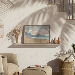 Puede incluir: Una pintura de acuarela enmarcada de un paisaje marítimo con una playa, montañas y un cielo nublado. La pintura está en un estante con dos jarrones y una jaula para pájaros.