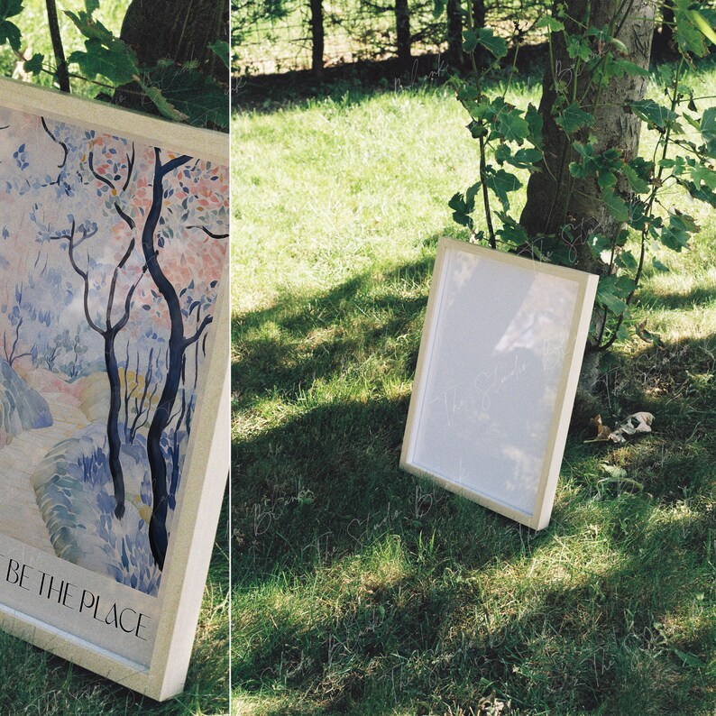 May include: Two white picture frames on a grassy lawn. The frame on the left has a watercolor painting of a blue and pink tree with the text "BE THE PLACE". The frame on the right is empty.
