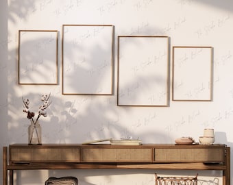 Op de afbeelding: Vier gouden fotolijsten in verschillende maten hangen aan een witte muur met een subtiel patroon. De lijsten zijn leeg en hebben een lichte reflectie. Een houten tafel met een geweven rotanblad staat voor de muur. De tafel heeft een geweven rotanmand en een stapel gevouwen handdoeken erop.