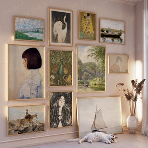 Könnte beinhalten: Eine Wandgalerie mit einer Auswahl an gerahmten Kunstwerken, darunter ein Gemälde einer Flusslandschaft, ein Porträt einer Frau, ein Pfau, ein sich küssendes Paar, ein Segelboot auf dem Wasser und eine Frau, die ein Buch liest. Die Galerie ist mit einer weißen Katze geschmückt, die auf dem Boden vor den Kunstwerken liegt.
