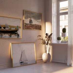 May include: Three framed paintings on a light pink wall with a window and white curtains in the background. The paintings are of a sailboat, a group of people in a boat, and two people walking on a beach.