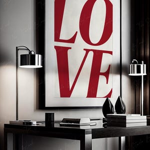 May include: A black framed poster with the word "LOVE" in large, bold, red letters on a white background. The poster is hanging on a wall above a black desk with a lamp on each side.