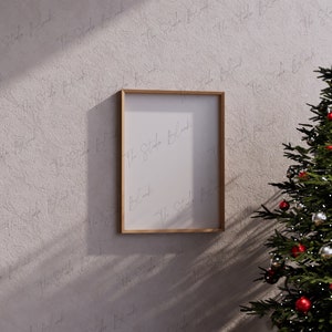 May include: A wooden frame with a white mat and a blank white canvas inside. The frame is hanging on a textured wall with a Christmas tree in the background.