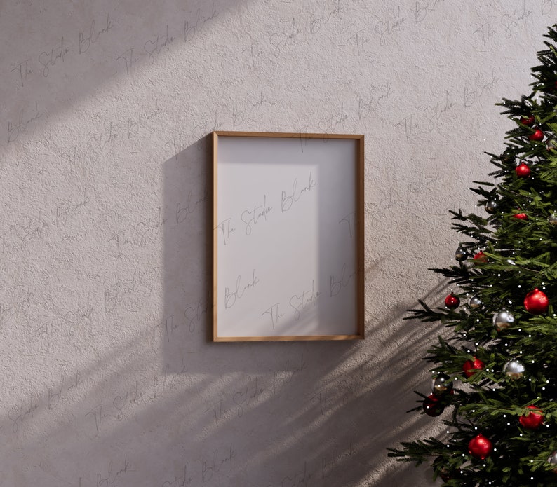 May include: A wooden frame with a white mat and a blank white canvas inside. The frame is hanging on a textured wall with a Christmas tree in the background.