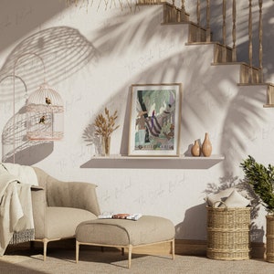 May include: A living room interior with a beige armchair, a beige ottoman, a birdcage with two birds, a framed print of a jungle scene, a shelf with a vase of dried flowers, and two wicker baskets with pillows.