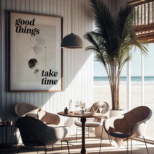 May include: A coastal-themed dining area with a round wooden table and four chairs. The chairs are upholstered in a light beige fabric. A framed print with the text "good things take time" hangs on the wall. A palm tree stands in a pot next to a large window overlooking a beach.