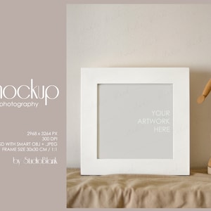 Peut inclure: Maquette de cadre photo blanc avec un fond gris clair. Le cadre est posé sur une surface en tissu brun. Un mannequin d'artiste en bois se tient à droite du cadre. Le texte "YOUR ARTWORK HERE" est visible dans le cadre.