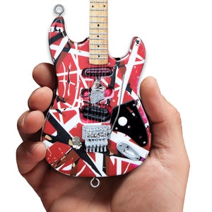 以下が含まれることがあります： 木製のネックと銀色のチューニングペグが付いた、赤、白、黒の電気ギターのミニチュアレプリカです。