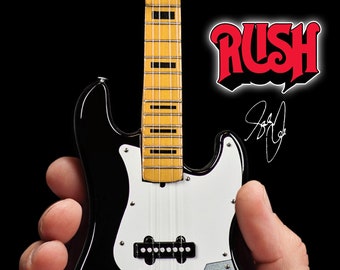 Op de afbeelding: Een zwarte en witte miniatuur elektrische basgitaar met een geel en zwart toets. De gitaar is gesigneerd "Geddy Lee". Het woord "RUSH" staat in rode letters boven de handtekening.