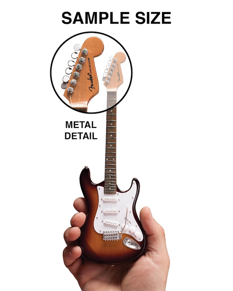 May include: A miniature replica of a Fender Stratocaster electric guitar, with a sunburst finish, white pickguard, and chrome hardware. The guitar is being held in a person's hand to show its size.