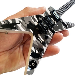 May include: A miniature electric guitar with a black and white camouflage design. The guitar has a black pickguard and black hardware. The guitar is held in a person's hand.