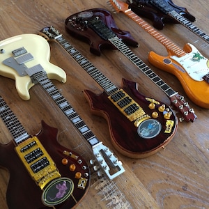 May include: Six electric guitars of various colours and styles, including a white guitar with a black pickguard, a brown guitar with gold hardware, and a yellow guitar with a white pickguard.