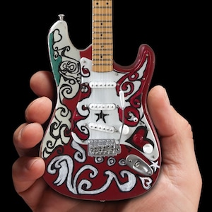May include: A red electric guitar with white and green painted designs. The guitar has a white pickguard with a black star and a silver pickup.