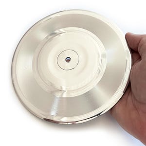 May include: A silver-coloured vinyl record with a centre hole. The record is smooth and shiny.