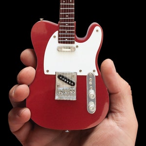 May include: A red electric guitar with a white pickguard and chrome hardware. The guitar is being held in someone's hand.