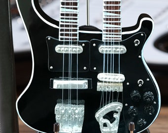 Op de afbeelding: Een zwarte elektrische gitaar met dubbele hals, chromen hardware en een zilveren slagplaat. De gitaar staat op een zwarte standaard.