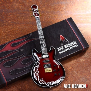 May include: A red electric guitar with white floral inlays on the body and neck. The guitar is in a black box with the text "Axe Heaven Miniature Guitars" on the side.