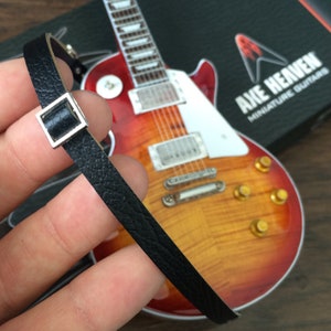 以下が含まれることがあります： 銀色のバックルが付いた黒い革のギターストラップ。ストラップは赤と黄色のエレキギターの上に置かれています。