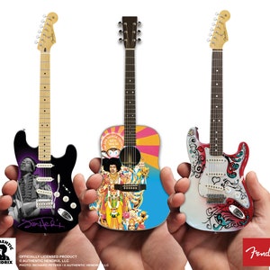 May include: Three miniature guitars, a black Fender Stratocaster with a Jimi Hendrix image, a blue and yellow acoustic guitar with a Jimi Hendrix image, and a white Fender Stratocaster with a psychedelic design. The guitars are held in the hands of a person.