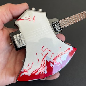 May include: A white and red axe-shaped electric guitar with a black pickguard and a wooden fretboard.