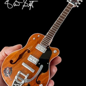 Puede incluir: Una guitarra el&eacute;ctrica marr&oacute;n y negra con una golpeador negro y un puente plateado. La guitarra tiene una pegatina de "Lucky Lady" en el cuerpo y una pegatina de gato negro con la palabra "Digsby" en el cuerpo. La guitarra tambi&eacute;n tiene dos dados blancos en el cuerpo.