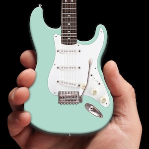 May include: A miniature electric guitar with a light blue body, white pickguard, and chrome hardware. The guitar has six strings and a single pickup.