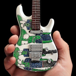 May include: A white electric guitar with a green, blue, and black abstract design. The guitar has a silver bridge and a brown fretboard.