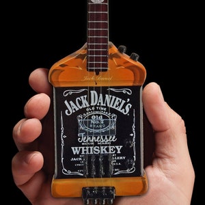 May include: A miniature guitar shaped like a Jack Daniel's whiskey bottle. The guitar has a black body with the Jack Daniel's label and a brown wooden neck with strings.