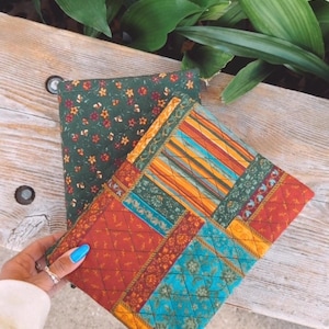 May include: Three fabric pouches with different patterns. The top pouch is green with small white flowers. The middle pouch is a patchwork of red, yellow, blue, and green. The bottom pouch is a solid red with a floral pattern.