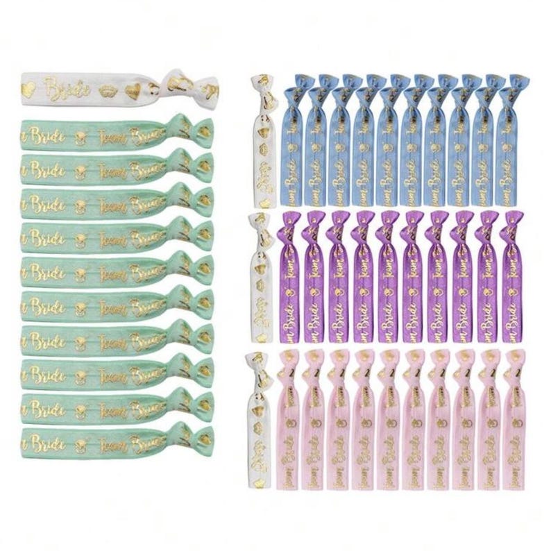 May include: Set of 40 hair ties with the text "Team Bride" in gold lettering on a variety of colored bands. The colors include light blue, purple, pink, and green.