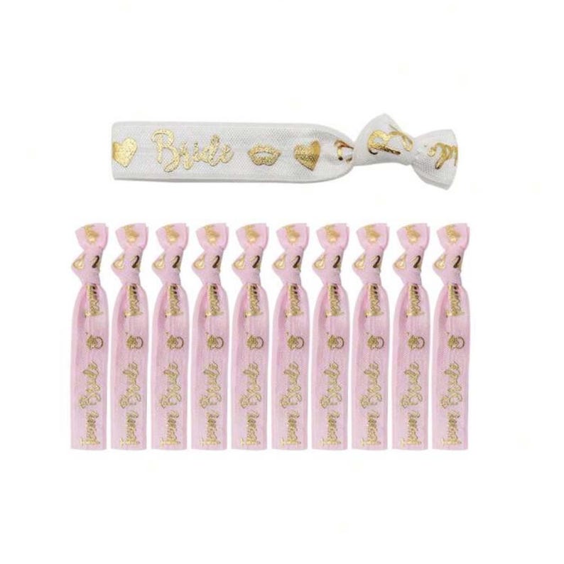 May include: Ten pink elastic hair ties with gold lettering that says "Bride Tribe" and a gold ring design. One white elastic hair tie with gold lettering that says "Bride" and gold crown and heart designs.