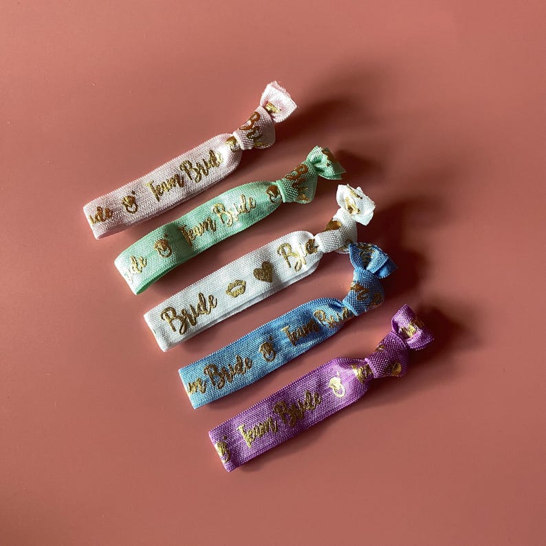 May include: Six colorful hair ties with gold lettering. The hair ties say "Team Bride" and "Bride".