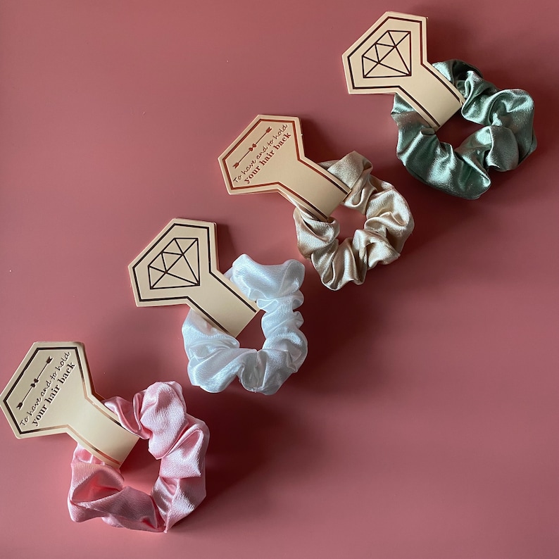 May include: Four satin scrunchies in different colors, each attached to a card with the text "To have and to hold your hair back". The cards are shaped like diamonds.