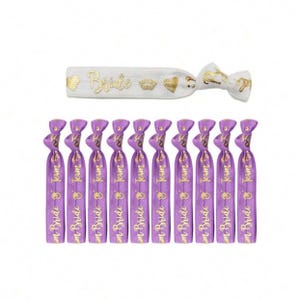 May include: Purple and white elastic hair ties with gold lettering. The purple hair ties say "Team Bride" and the white hair tie says "Bride".