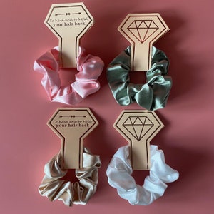 May include: Four hair scrunchies in different colors, pink, green, beige, and white, with a wooden sign that says "To have and to hold your hair back".