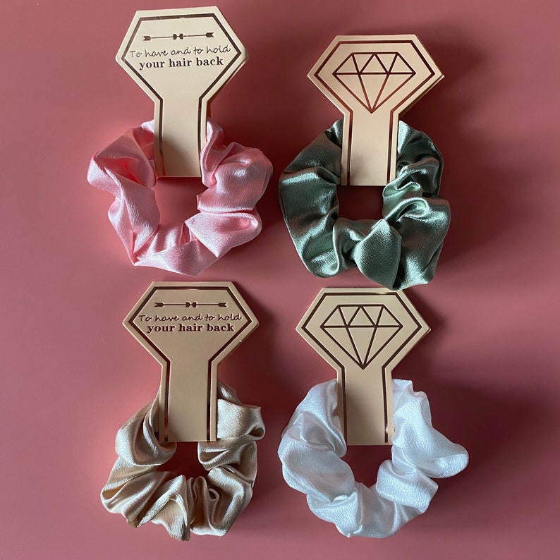 May include: Four hair scrunchies in different colors, pink, green, beige, and white, with a wooden sign that says "To have and to hold your hair back".