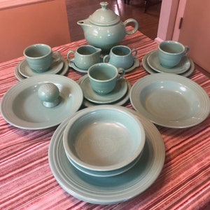 May include: A set of turquoise blue ceramic dishes, including a teapot, creamer, sugar bowl, cups, saucers, bowls, and plates. The dishes are arranged on a striped tablecloth.