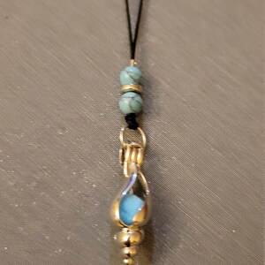 Puede incluir: Un collar con un colgante de piedra turquesa engastado en plata y dos cuentas turquesas en un cordón negro.