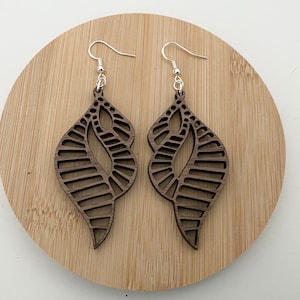 Puede incluir: Un par de pendientes de madera marrón con un diseño de hoja geométrico. Los pendientes cuelgan de ganchos plateados.