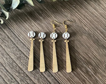 May include: Four pairs of wooden baseball bat earrings with a white baseball charm. The earrings are gold-toned and have a dangle style.