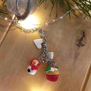 May include: A silver charm bracelet with a snowman, cupcake, and heart charms. The bracelet is attached to a silver tea ball.