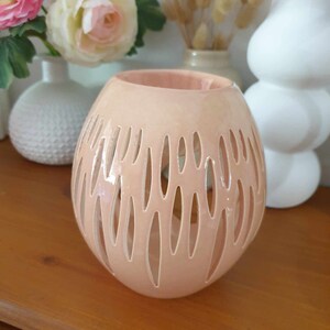Peut inclure: Un bougeoir en céramique rose pâle avec un motif découpé décoratif. Le bougeoir a une forme ronde et est fait d'un matériau lisse et brillant.