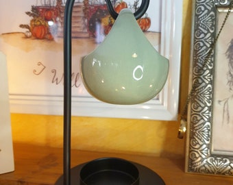 May include: A black metal candle holder with a teal ceramic oil burner hanging from a curved arm. The holder has a round base and a small candle cup.