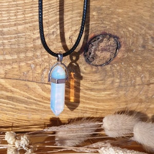 Puede incluir: Un colgante de cristal de ópalo blanco en un collar de cordón de cuero negro. El colgante es un cristal facetado puntiagudo con un engaste plateado.